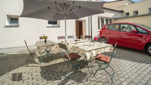 An outdoor patio with a table and chairs, a large umbrella, and a red car parked nearby. - Penzion Fan (Karlovy Vary)