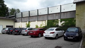 A parking lot with several cars parked in front of a building with a metal roof and a wall with bird silhouettes. - Penzion Fan (Karlovy Vary)