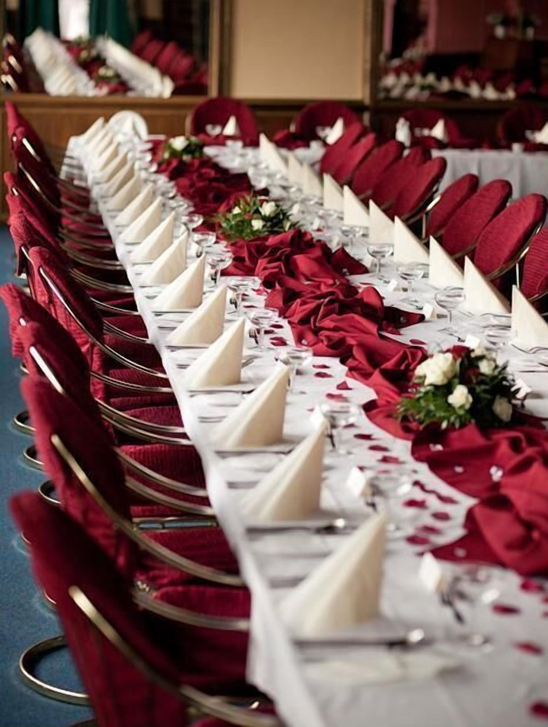 Une longue table dressée pour un événement formel, avec des chaises rouges et des serviettes blanches.