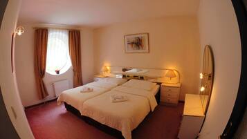 A hotel room with a large bed, bedside lamps, a window with curtains, a radiator, and a painting on the wall.
