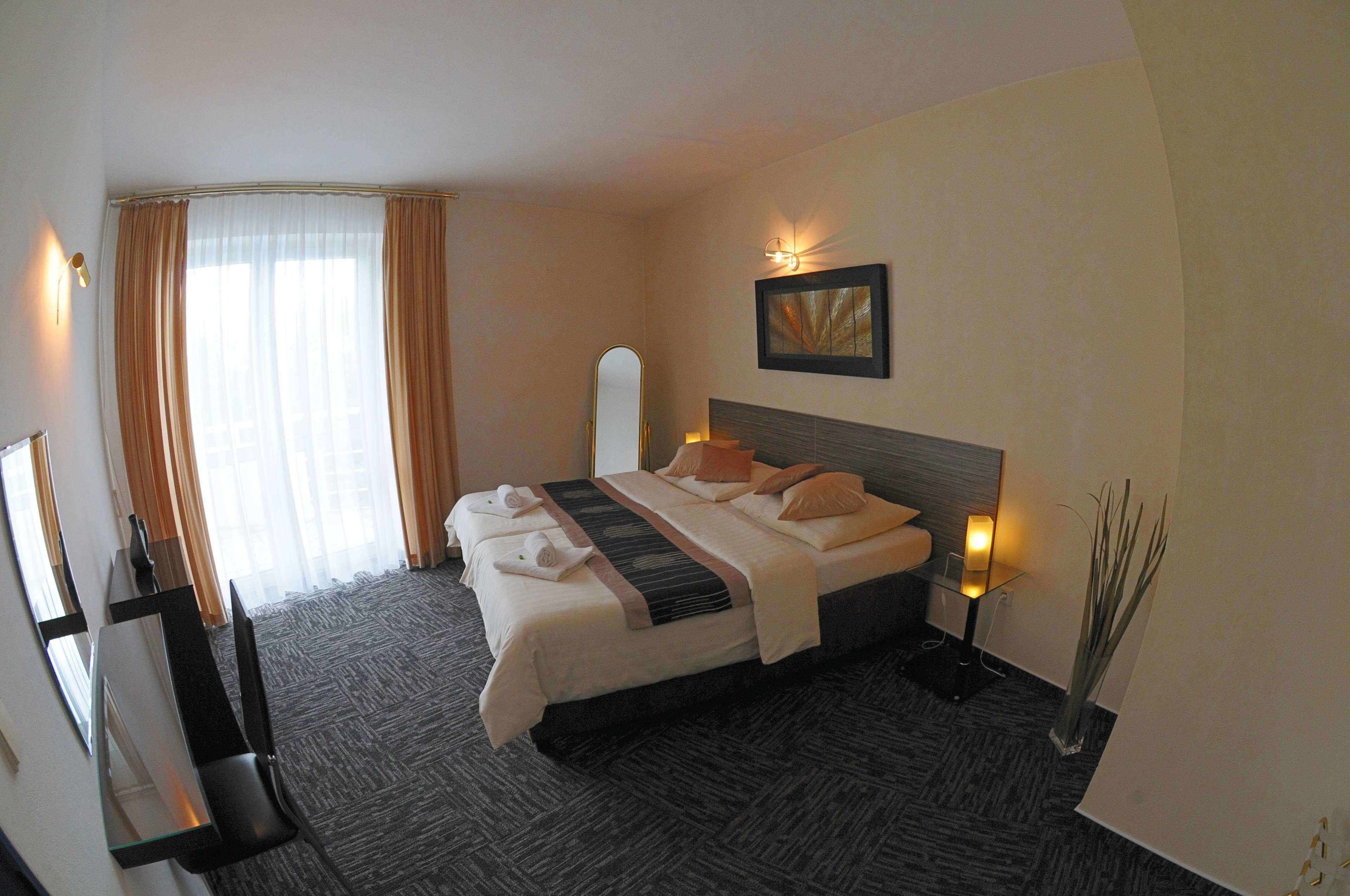 A hotel room with a large bed, a bedside table with a lamp, a mirror, and a painting on the wall.