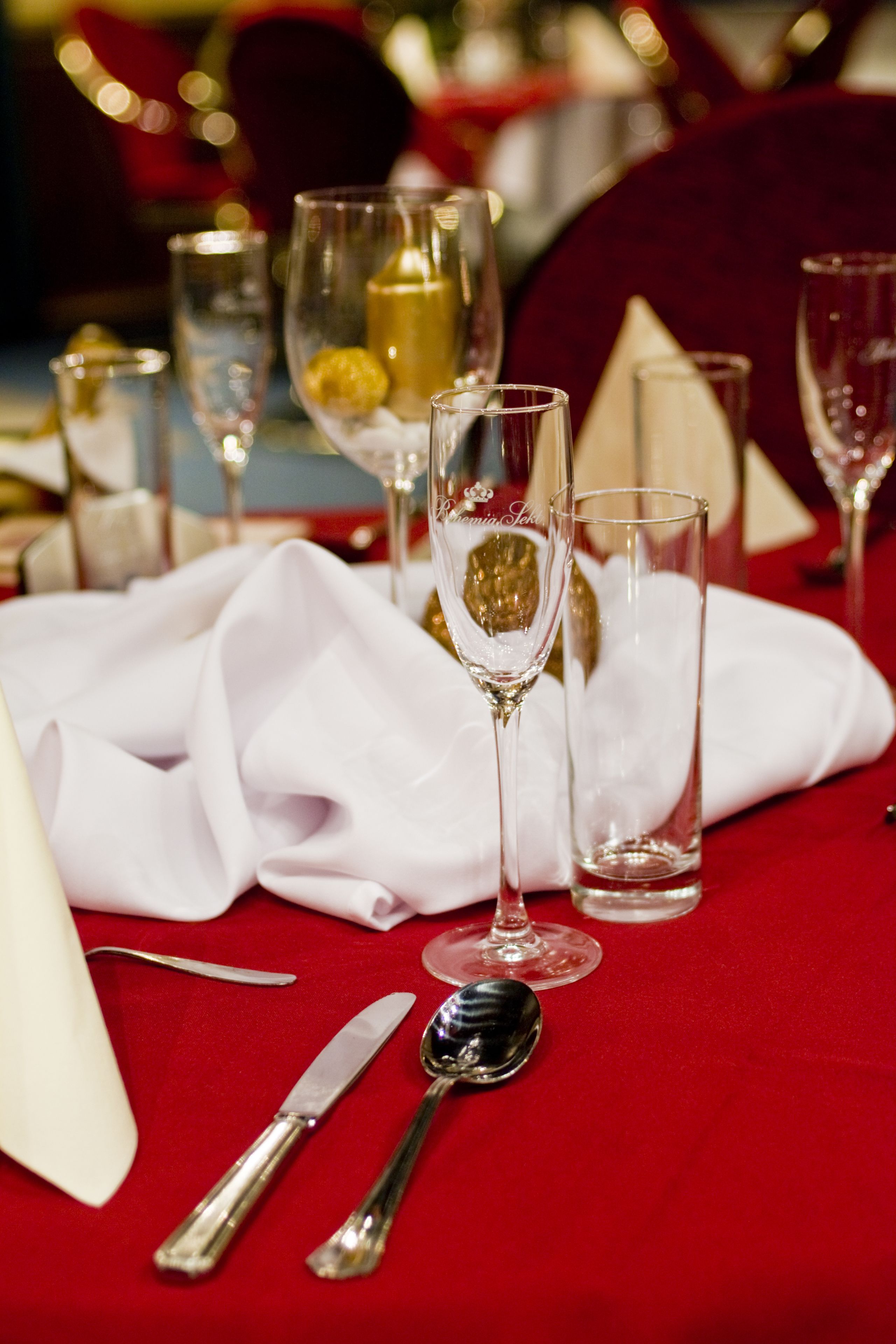 A table set with fine dining utensils, including a knife, spoon, and a folded napkin, on a red tablecloth.
