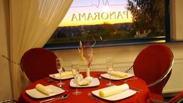 Mesa para dos personas dispuesta con mantel rojo, servilletas blancas y copas de vino.