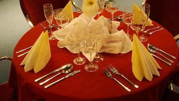 A round table set for a formal dinner with red tablecloth, white napkins, and silverware.
