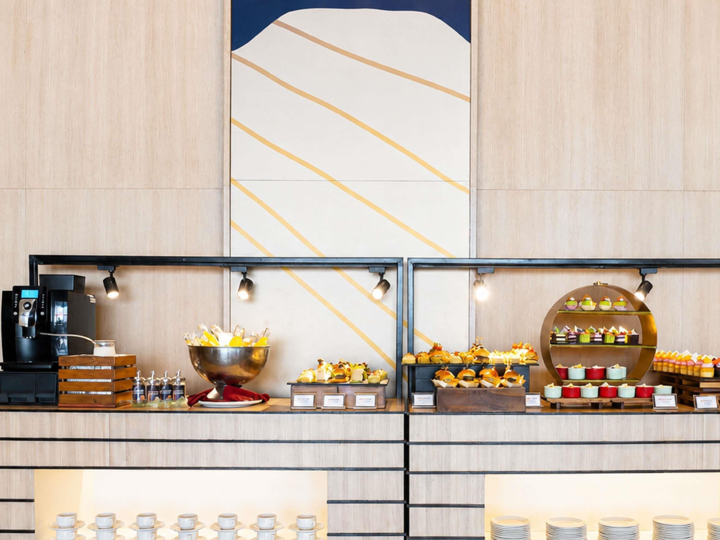 A buffet setup with a coffee machine, a large bowl of food, and various food items displayed on shelves.