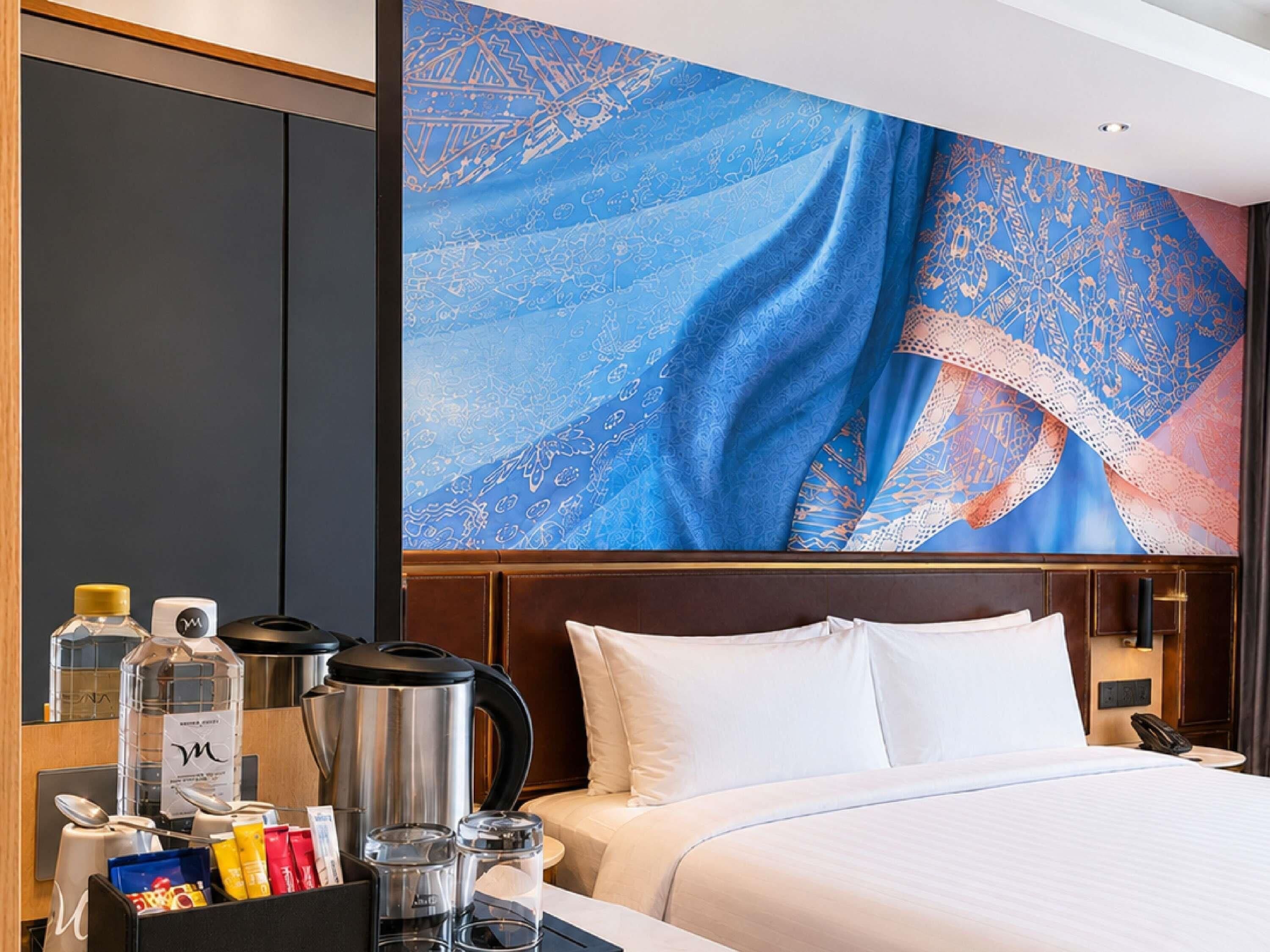 A hotel room with a large bed, a coffee maker, a kettle, and a breakfast bar with various items.