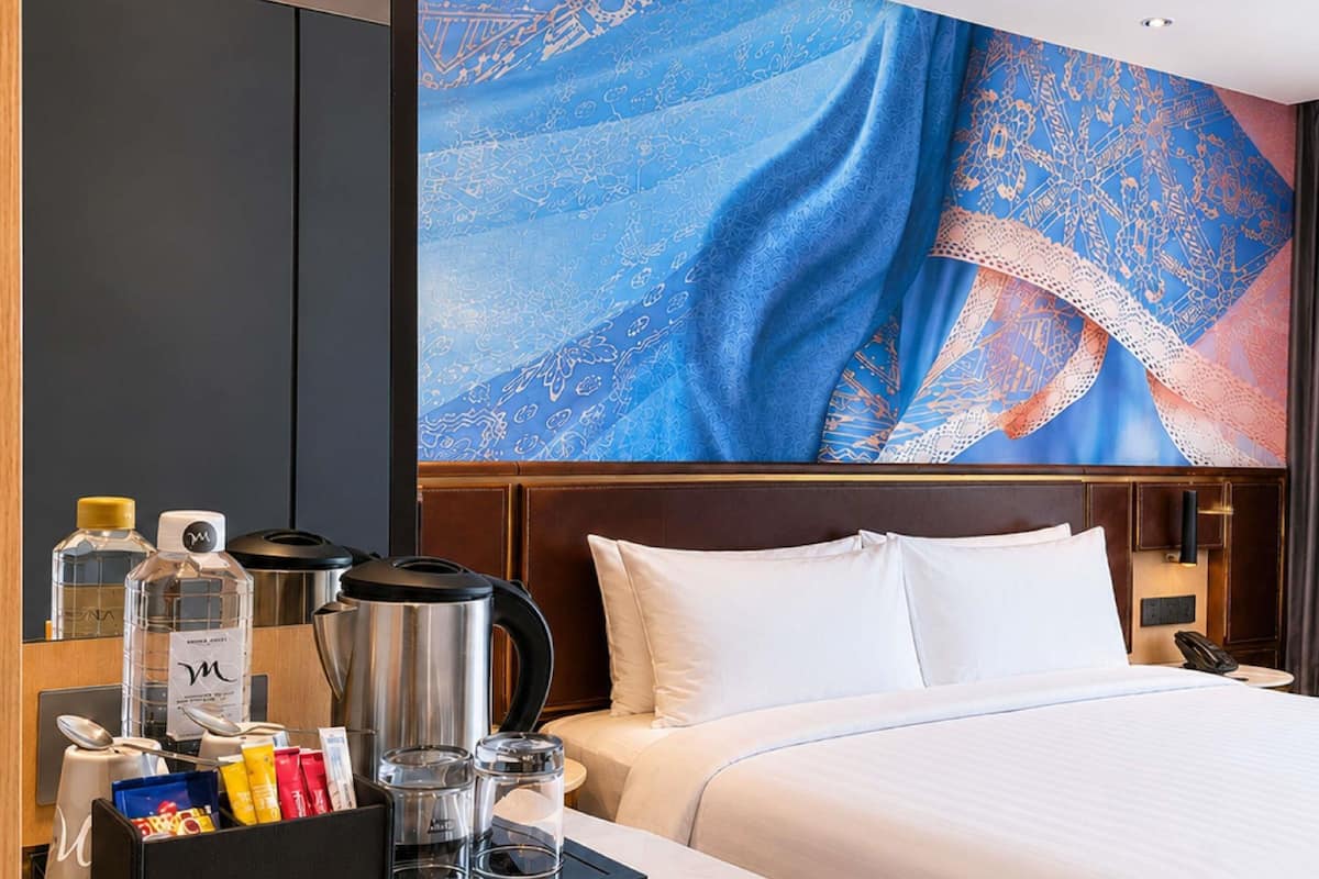 Quarto de hotel com uma cama grande, máquina de café, chaleira e um balcão de café da manhã com diversos itens.