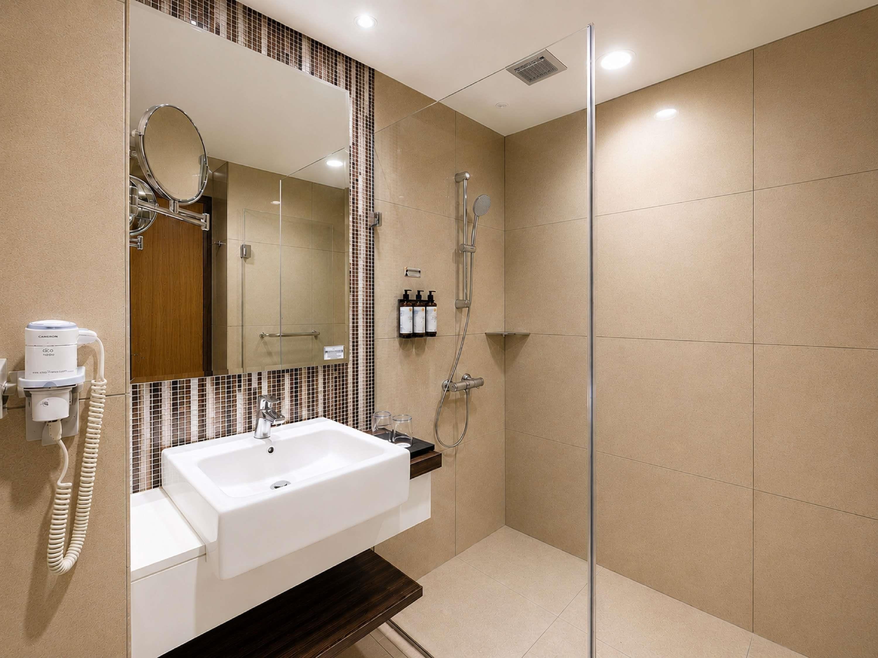 A modern bathroom with a white sink, a large mirror, a glass-enclosed shower, and a hand dryer.