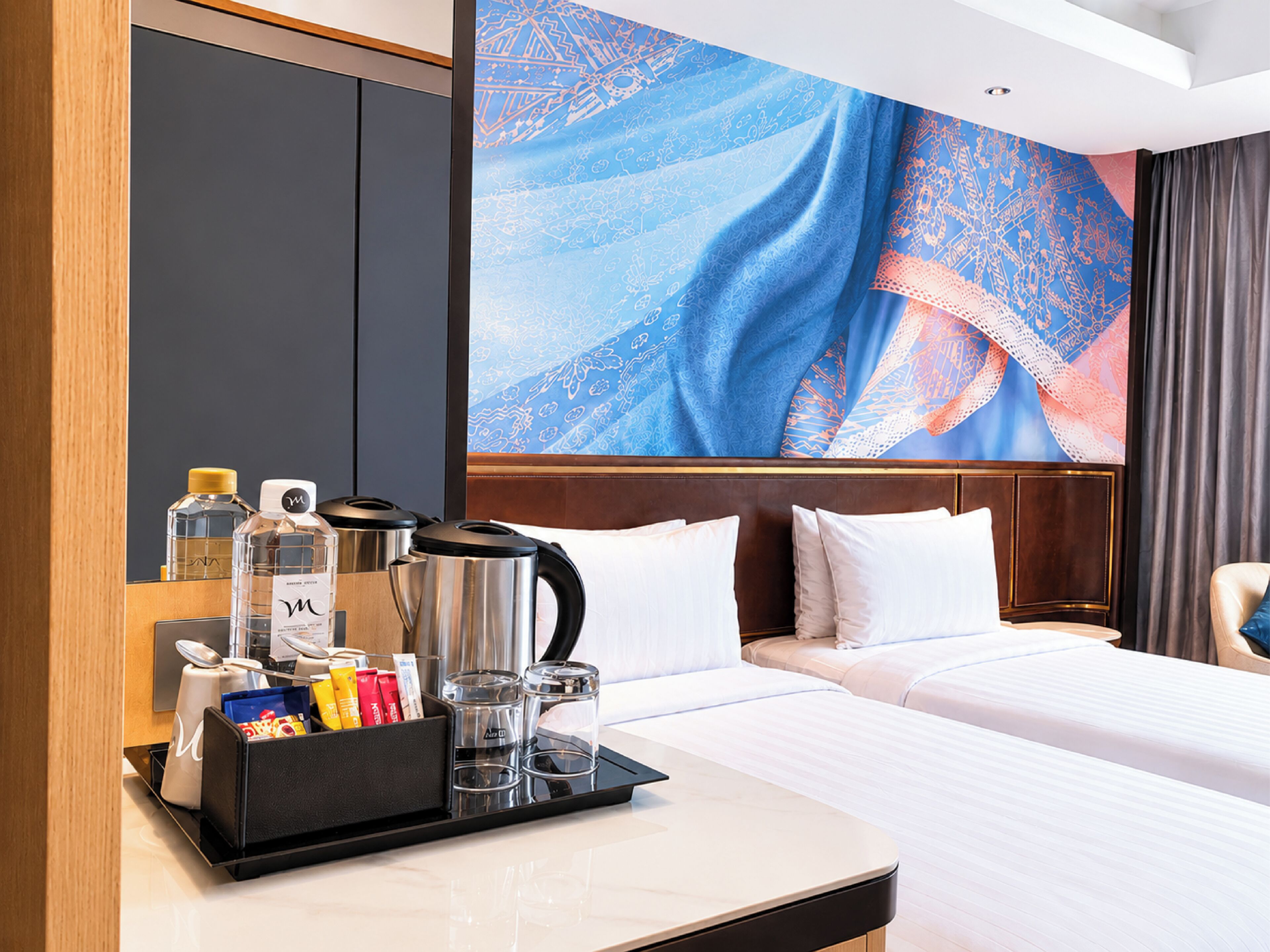 A hotel room with a bed, a bedside table with amenities, a large decorative wall, and a wooden headboard.