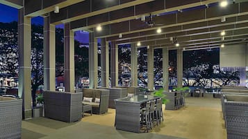 Un espacio al aire libre con mobiliario de mimbre y vistas a la ciudad iluminada de noche.
