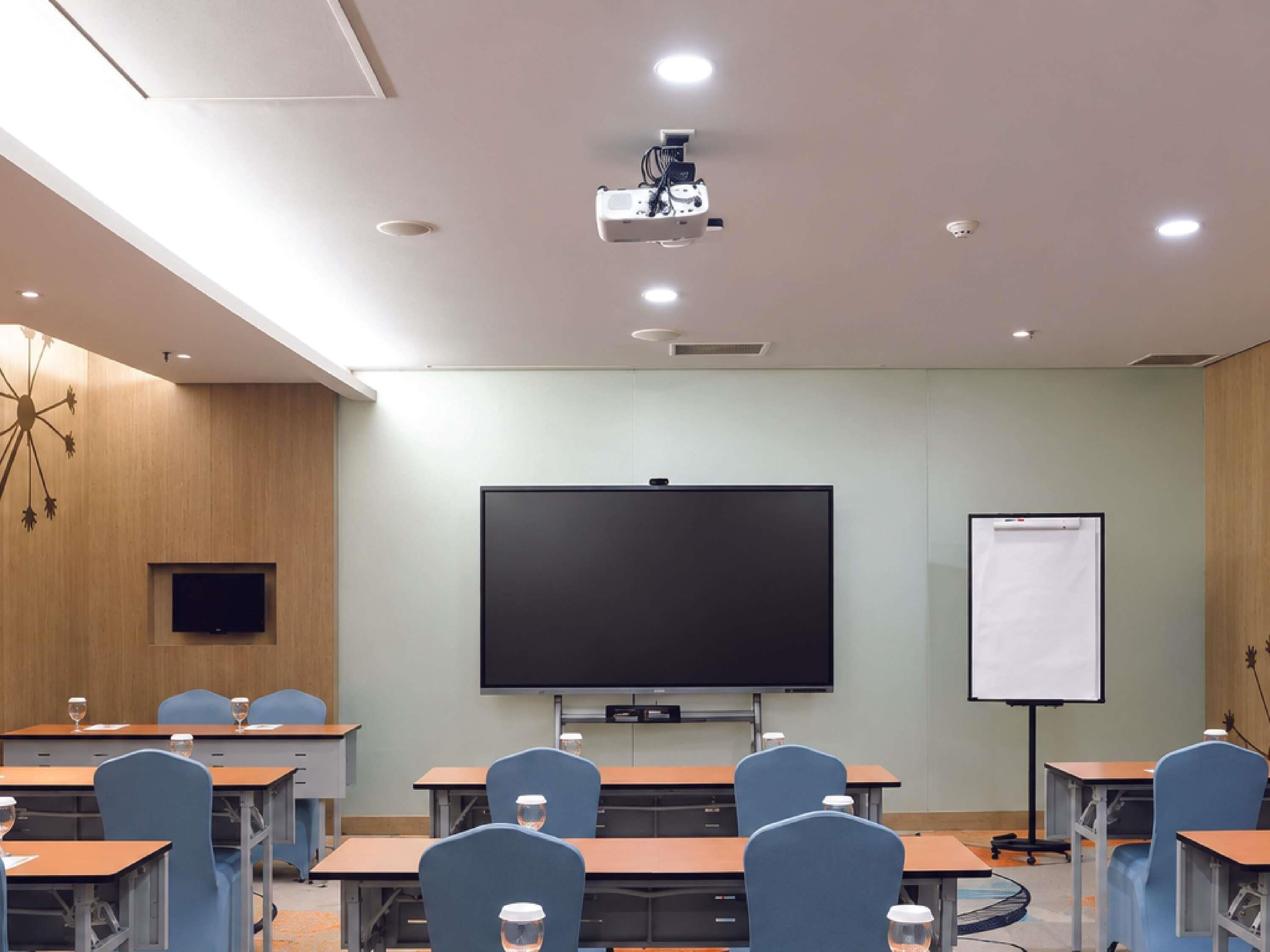 A conference room with a large screen, a whiteboard, and multiple tables with chairs.
