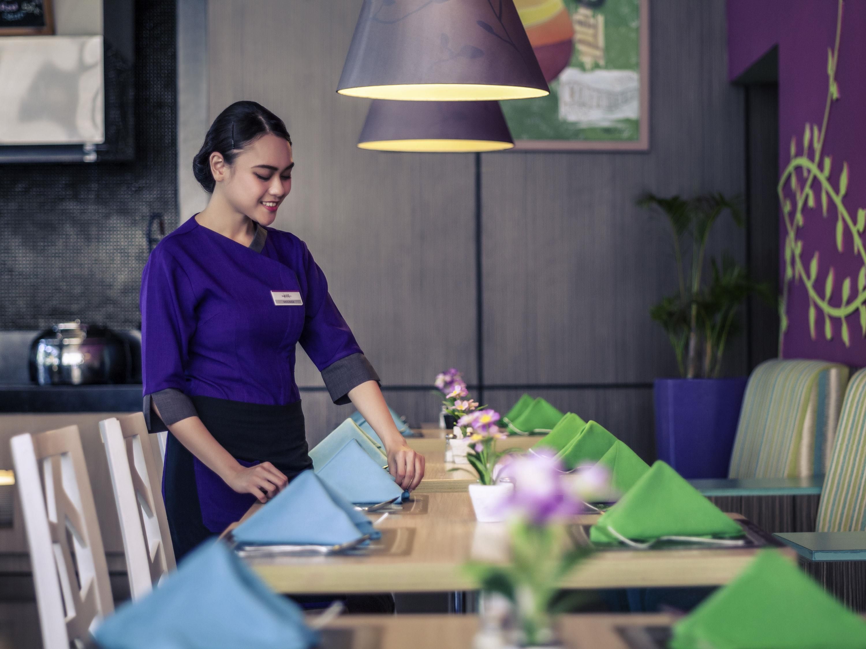 A restaurant setting with a waiter arranging blue napkins on a table.