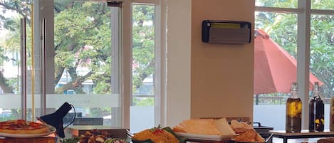 A buffet table with various dishes and a view of trees through large windows.