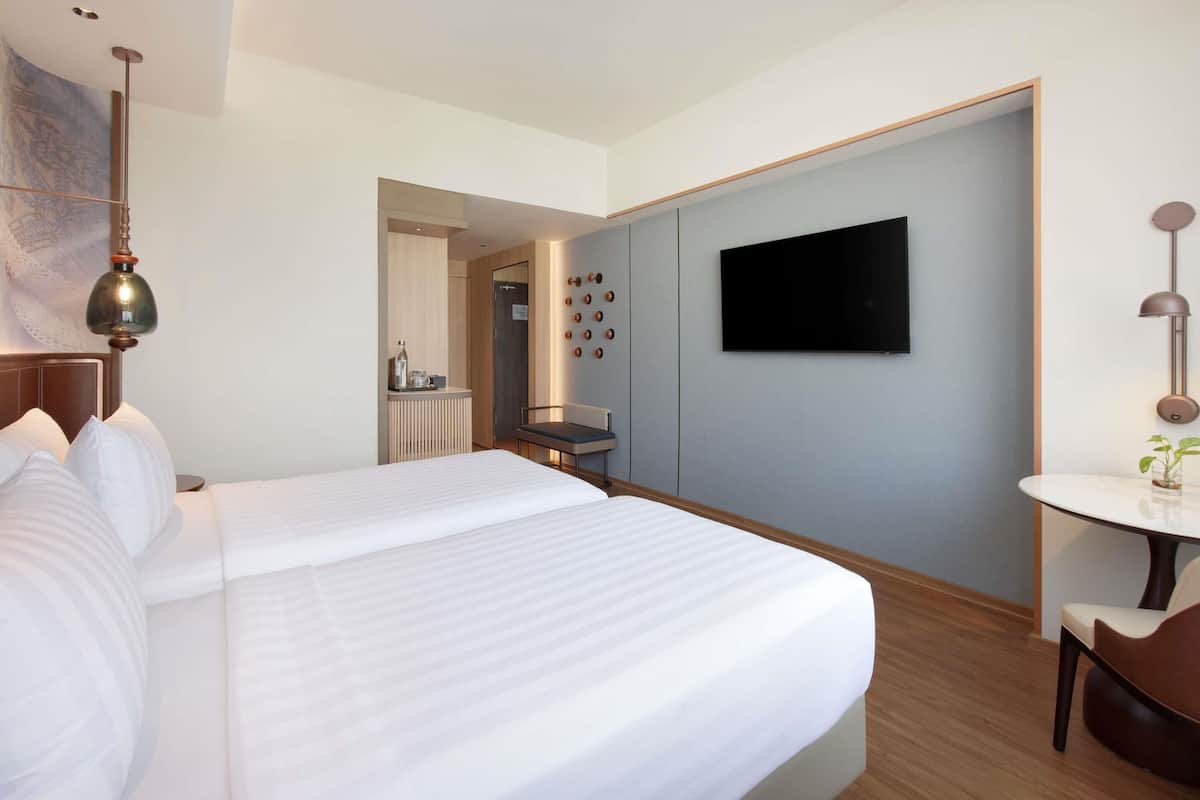 Habitación de hotel con una cama grande, un televisor montado en la pared, un escritorio con una silla y una mesita con una planta.