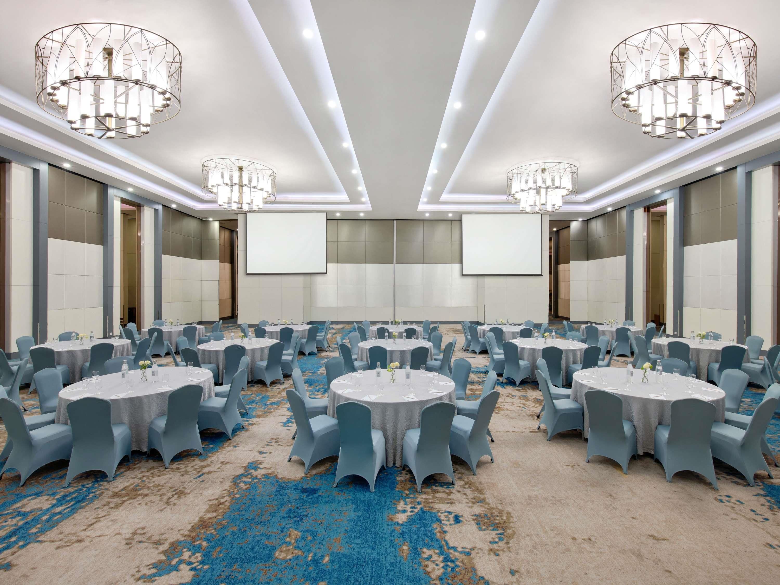 A conference room with round tables, blue chairs, and chandeliers.