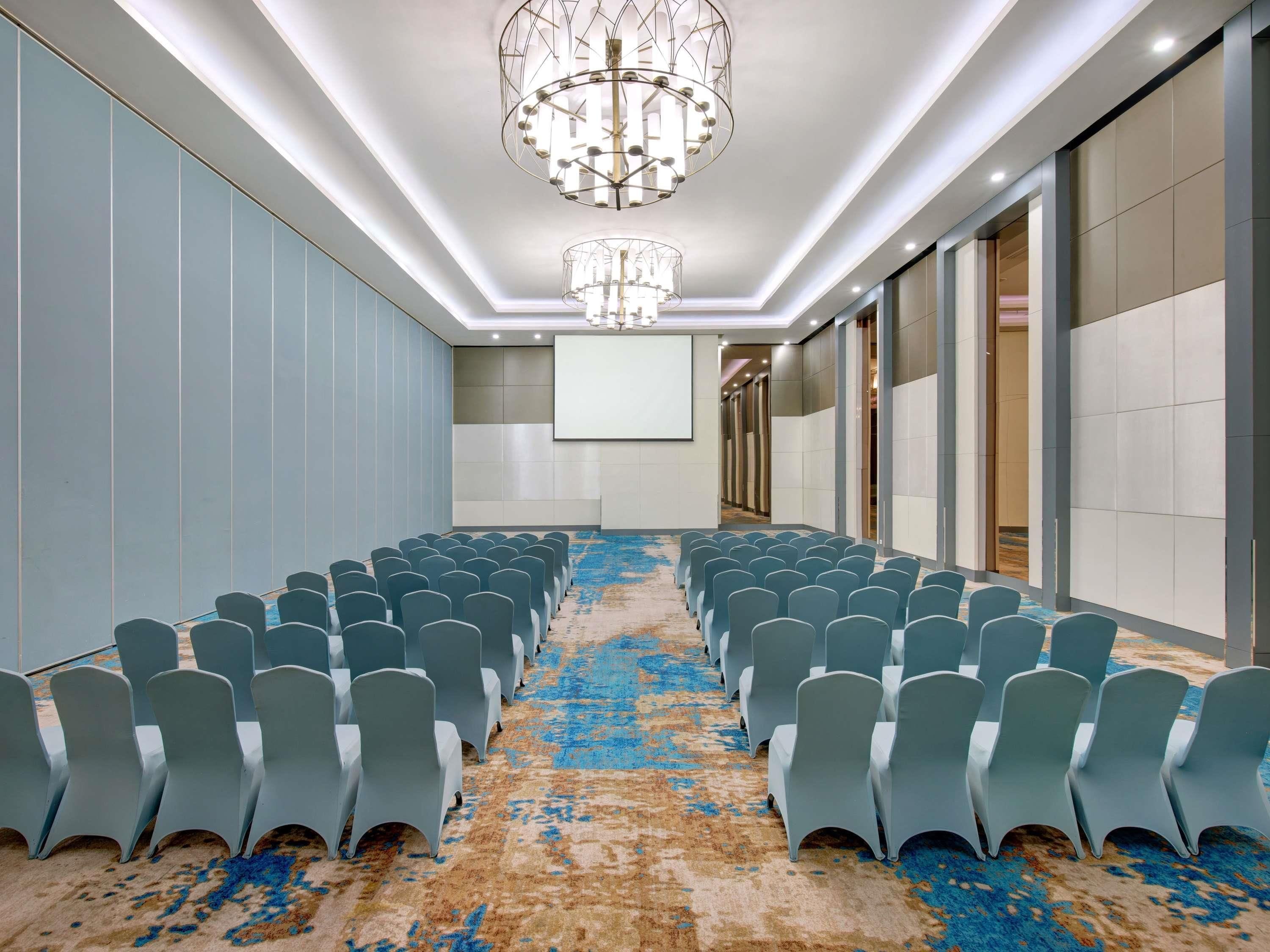 A conference room with rows of chairs, a projector screen, and a carpeted floor.