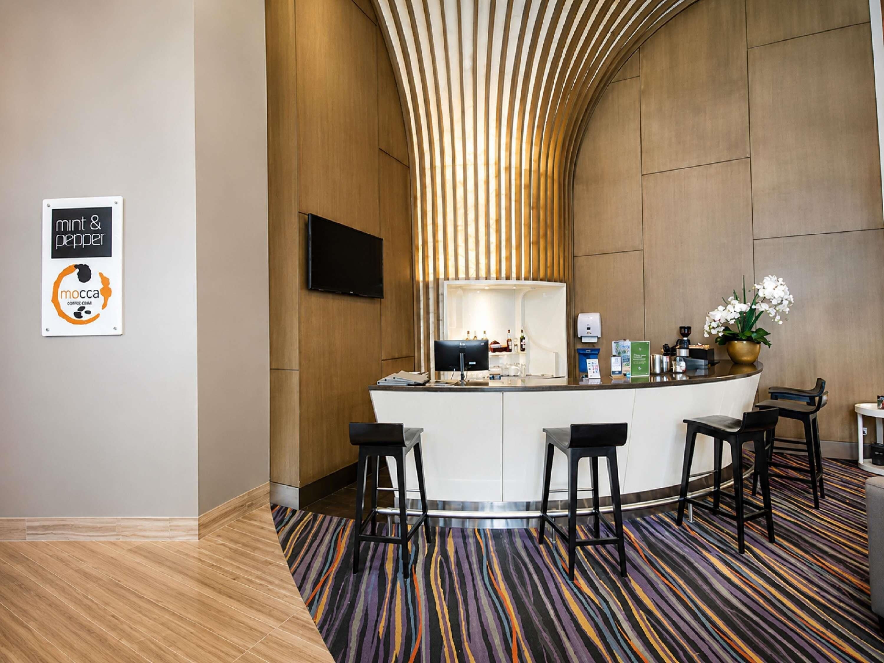 Un espace d’accueil moderne doté d’un mur en bois incurvé, d’un téléviseur à écran plat, d’un coin café et d’une moquette à motifs.