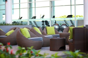 A modern outdoor seating area with wicker furniture and green cushions, overlooking a fitness center with exercise equipment.