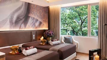 A hotel room with two beds, a large window with a view of trees, a painting on the wall, and a small table with amenities.