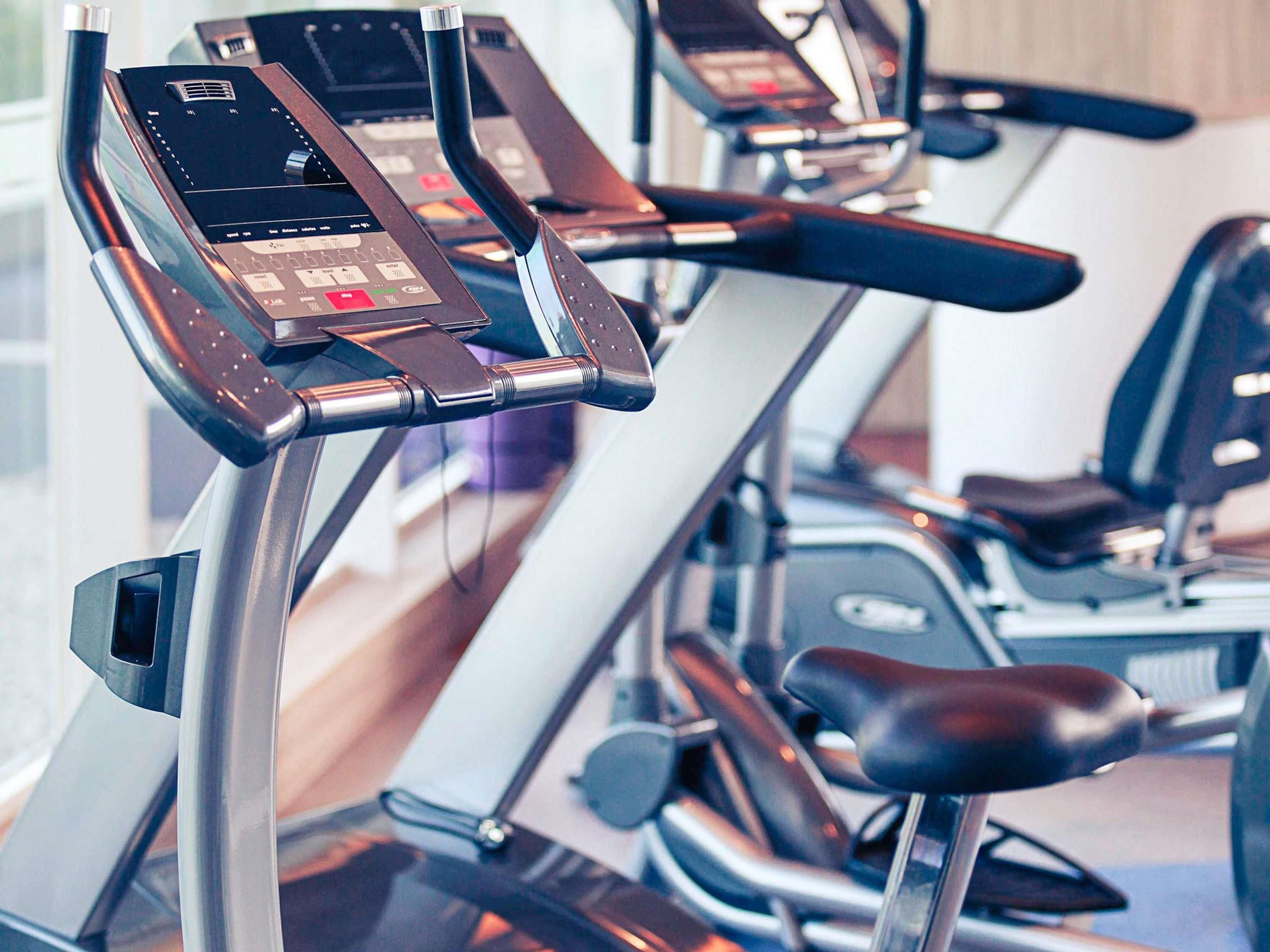 A row of stationary exercise bikes with digital displays and control panels, likely in a gym setting.