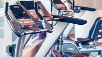 A row of stationary exercise bikes with digital displays and control panels, likely in a gym setting.