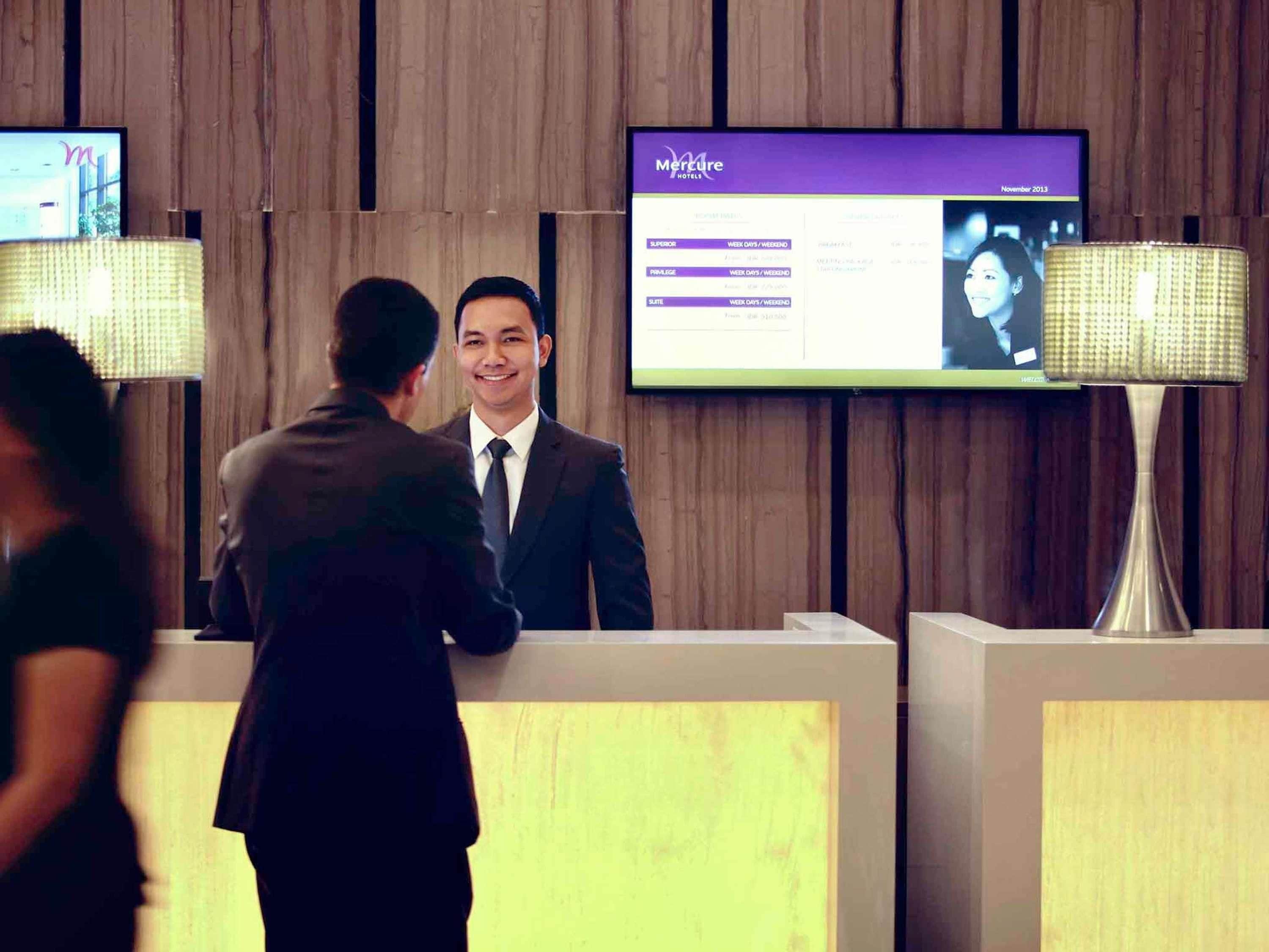 Een receptiebalie van een hotel met een digitaal scherm dat prijzen en data toont.