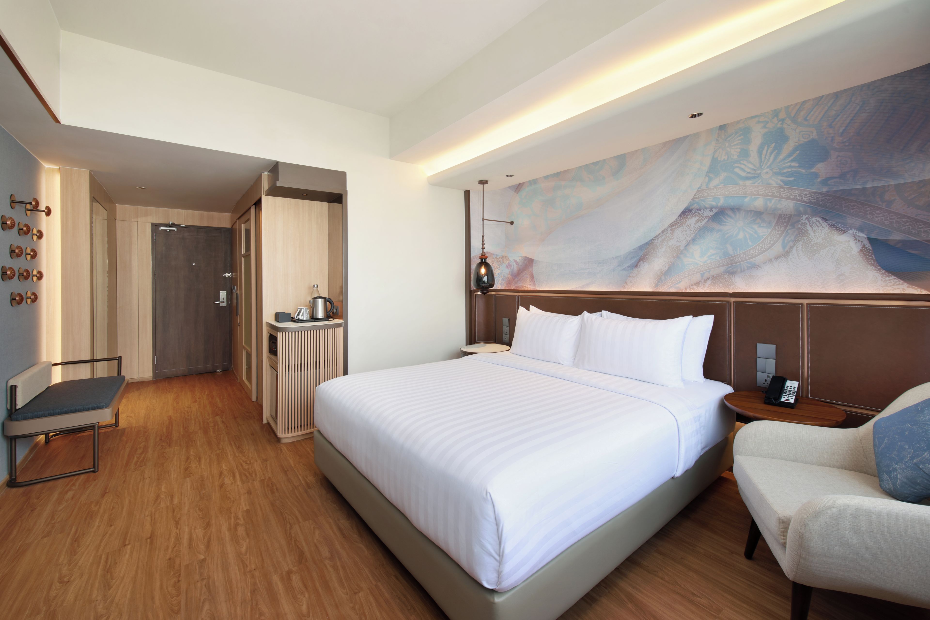 A hotel room with a large bed, a desk, a chair, a coffee machine, and a wall-mounted lamp.