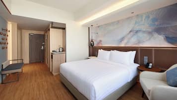 A hotel room with a large bed, a desk, a chair, a coffee machine, and a wall-mounted lamp.