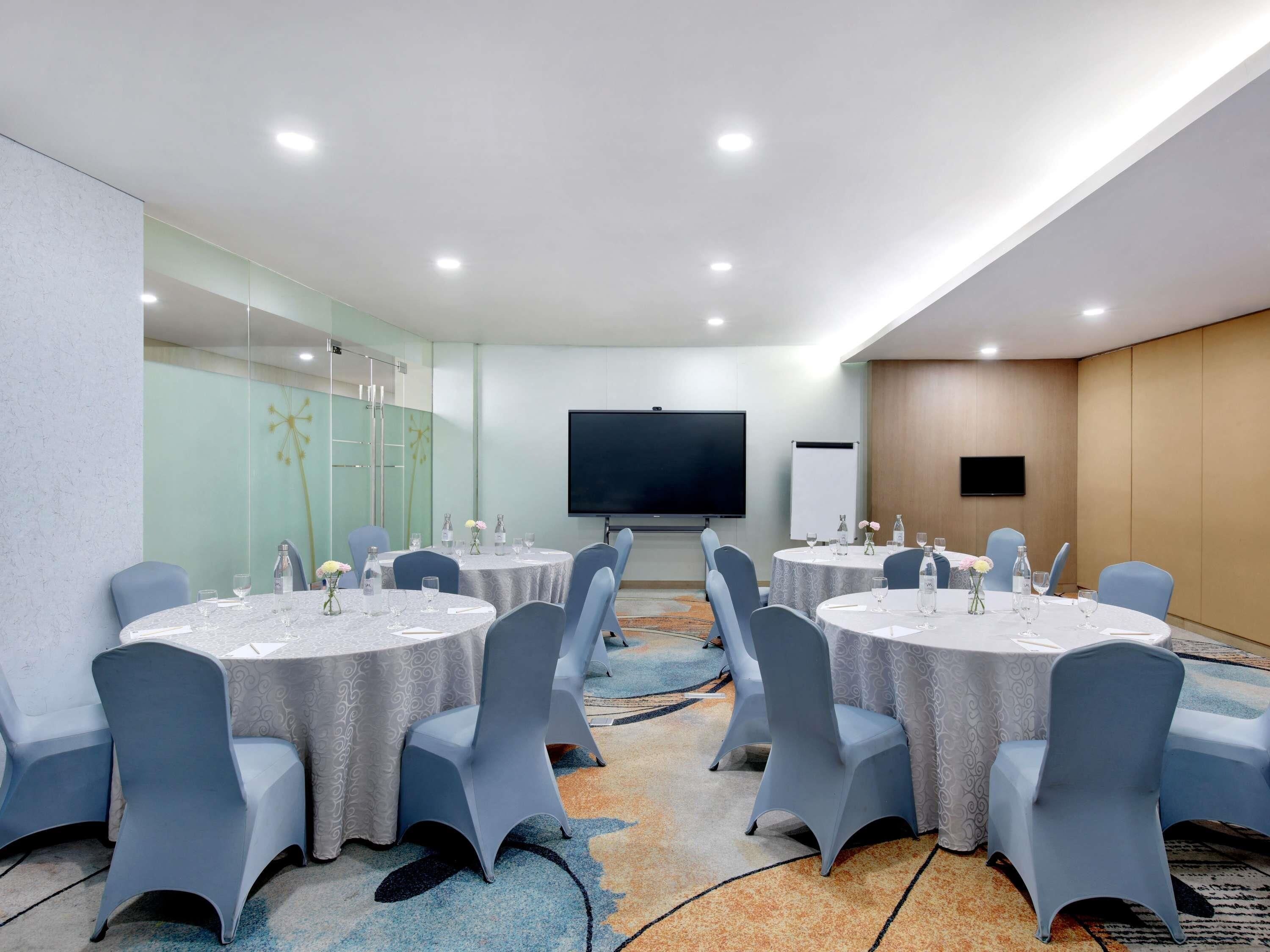 A conference room with round tables, chairs, a projector screen, and a whiteboard.