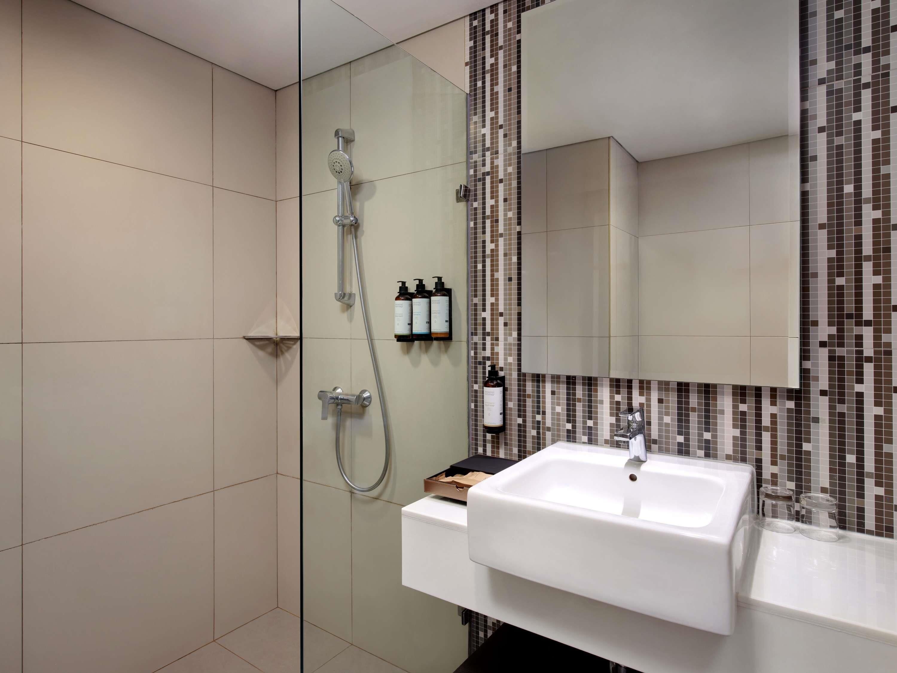 A modern bathroom with a glass shower enclosure, a white sink, and a tiled backsplash.