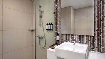 Un baño moderno con cabina de ducha de vidrio, un lavabo blanco y un salpicadero de azulejos.