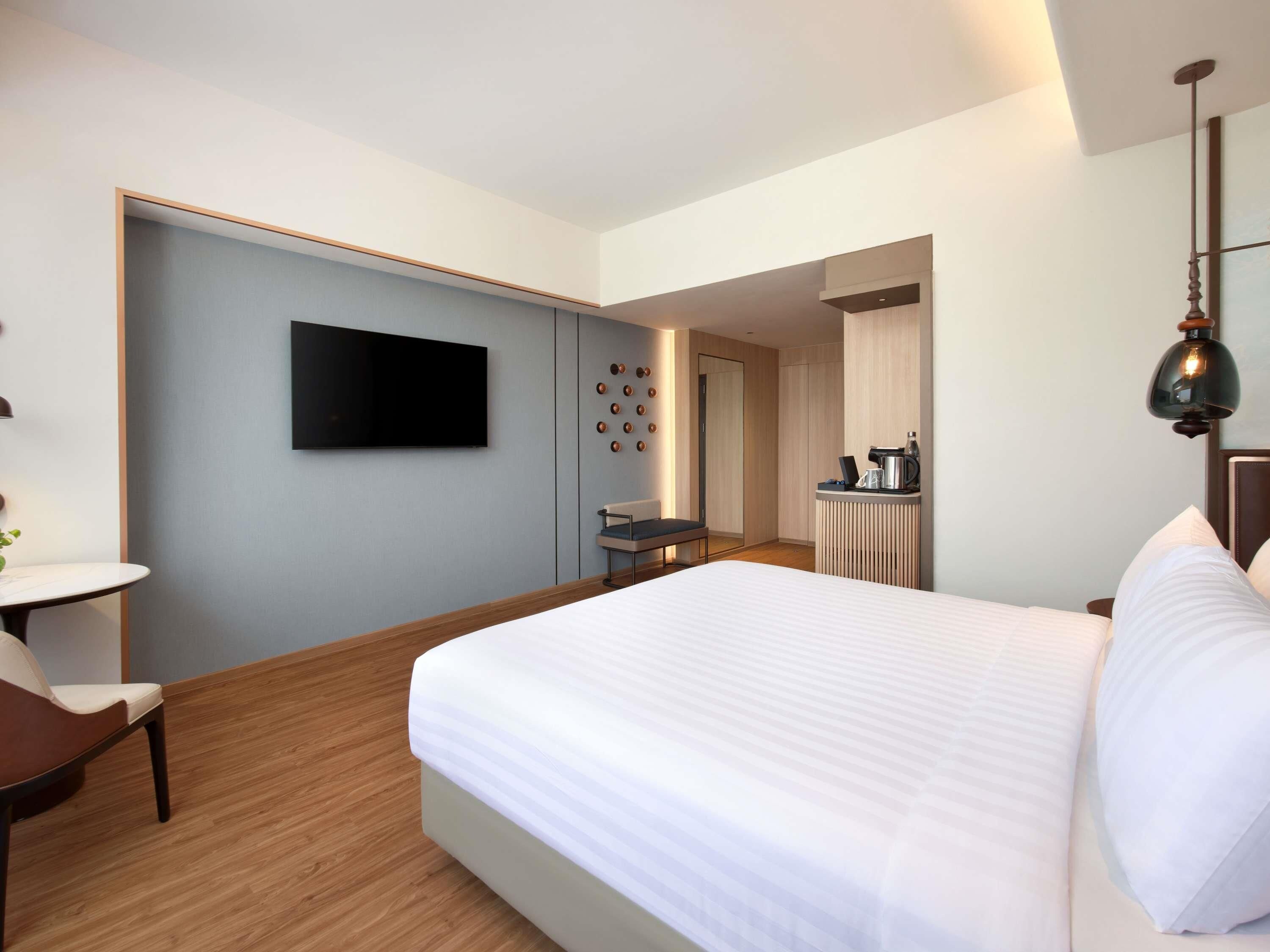 A hotel room with a bed, a desk, a chair, a TV, a coffee maker, and a mirror.