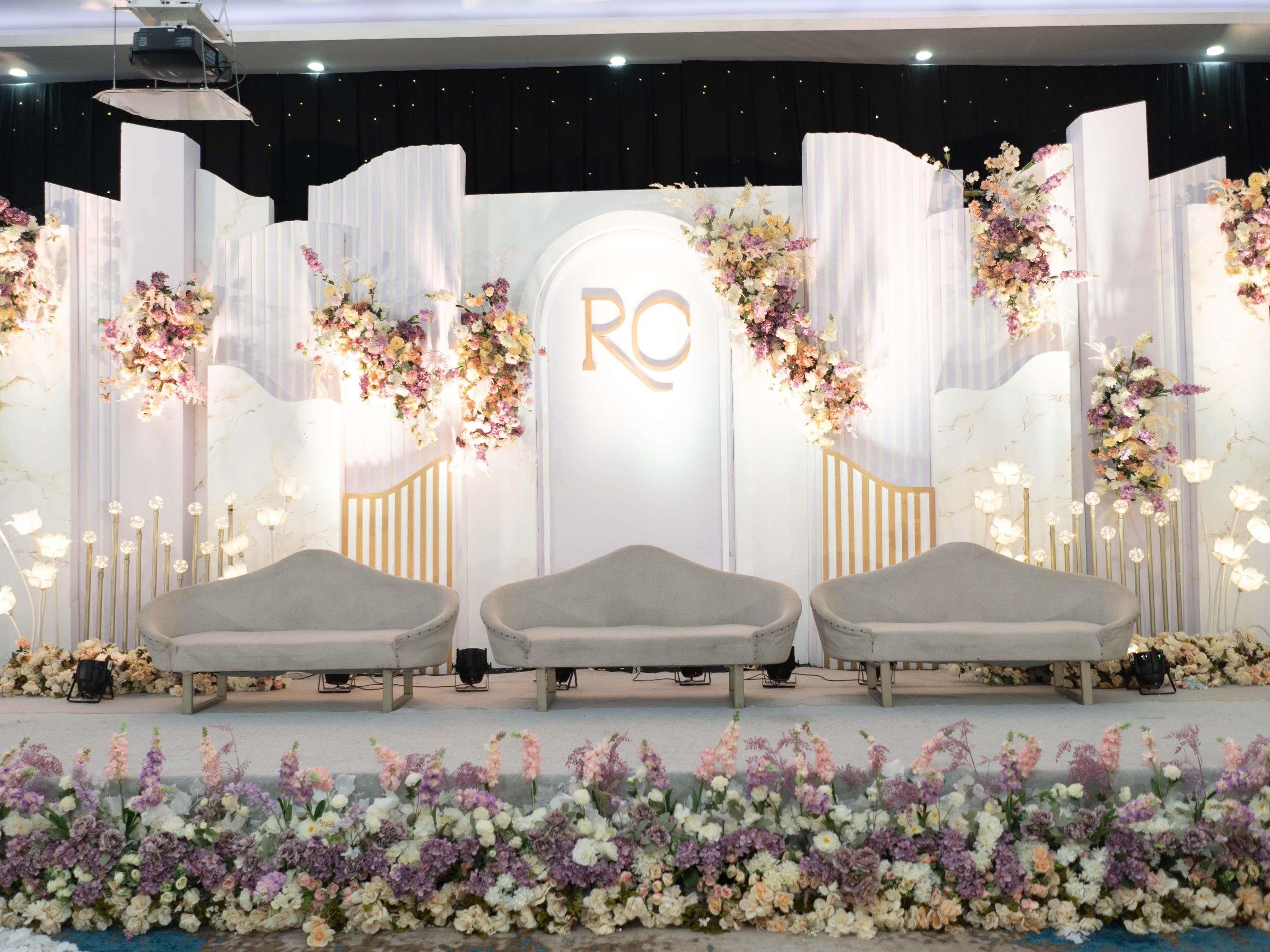 A stage with three grey chairs, a floral backdrop, and a central sign with 'RO' illuminated.