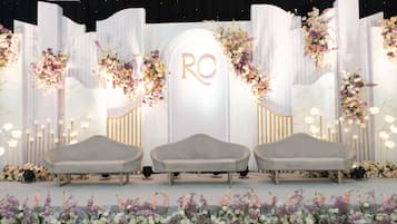 A stage with three grey chairs, a floral backdrop, and a central sign with 'RO' illuminated.