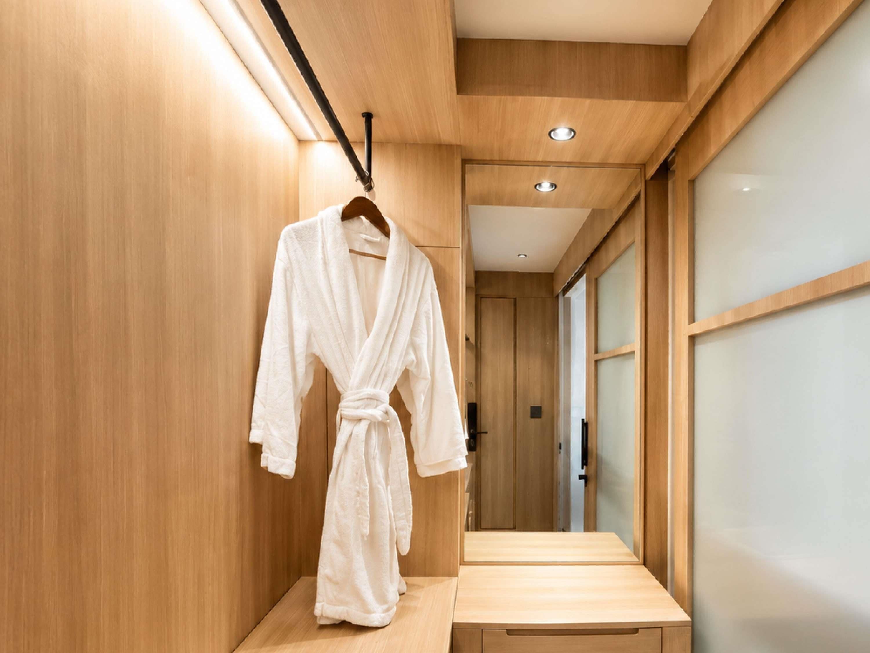 A wooden interior hallway with a white robe hanging on a rack, a wooden bench, and a door leading to another room.