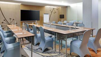 A conference room with tables, chairs, a projector screen, and a whiteboard.