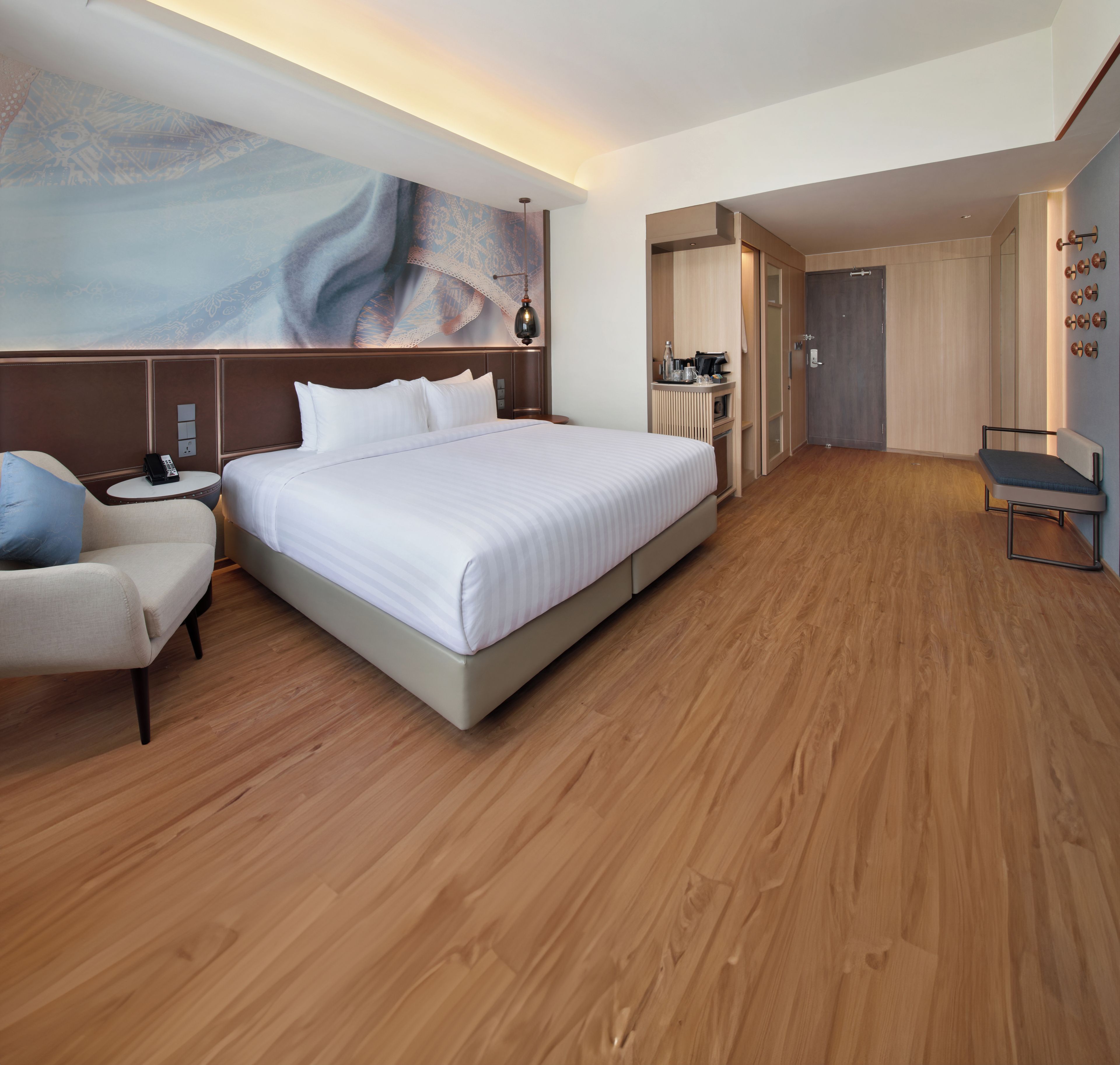 A hotel room with a large bed, a desk, a chair, and a wardrobe.