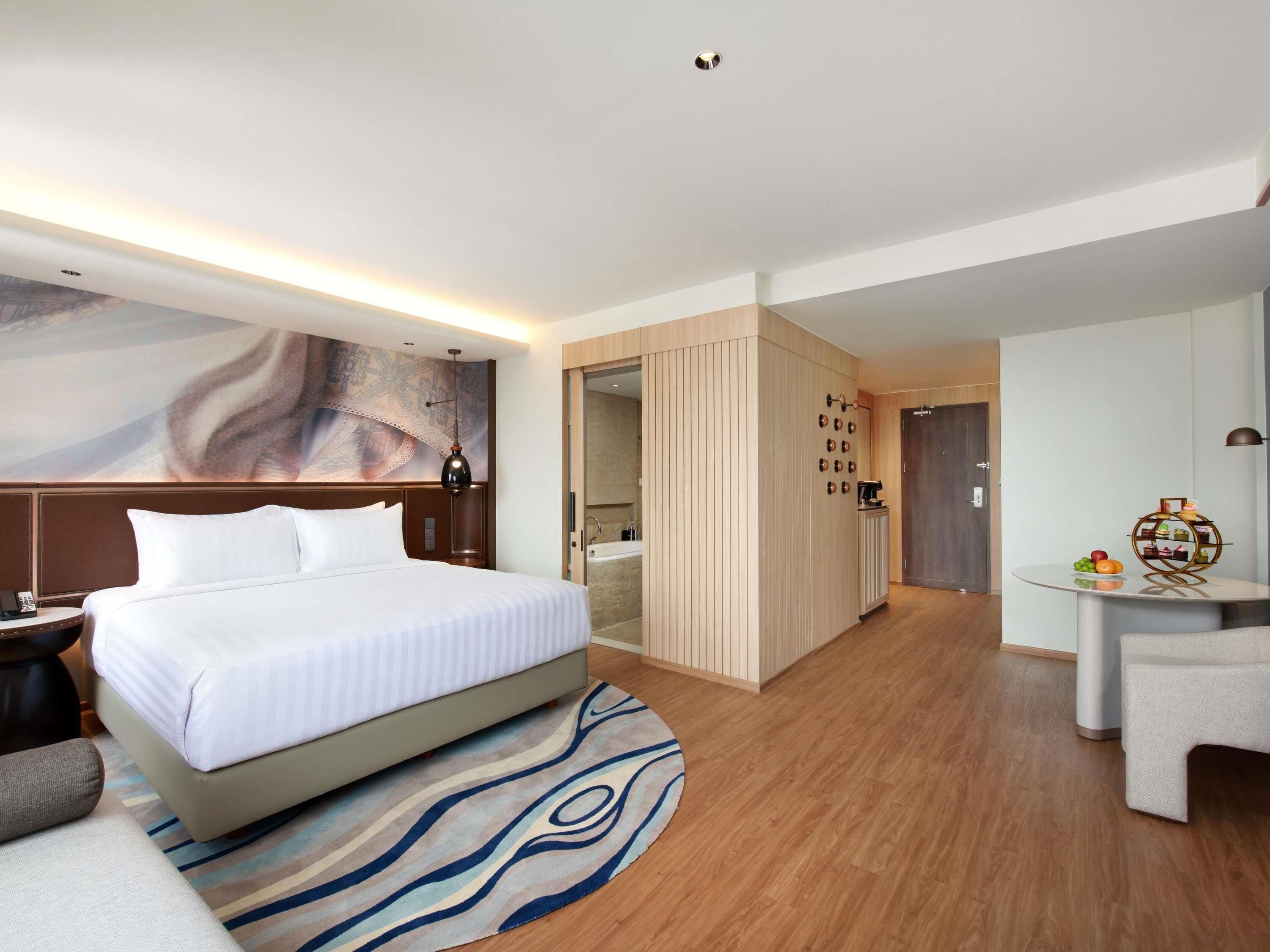 Une chambre d’hôtel comprenant un lit, un bureau, une chaise, une horloge fixée au mur et une porte donnant accès à une salle de bain.