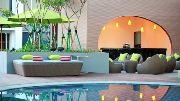Un área de lounge exterior moderna con piscina, asientos con cojines y sombrillas.