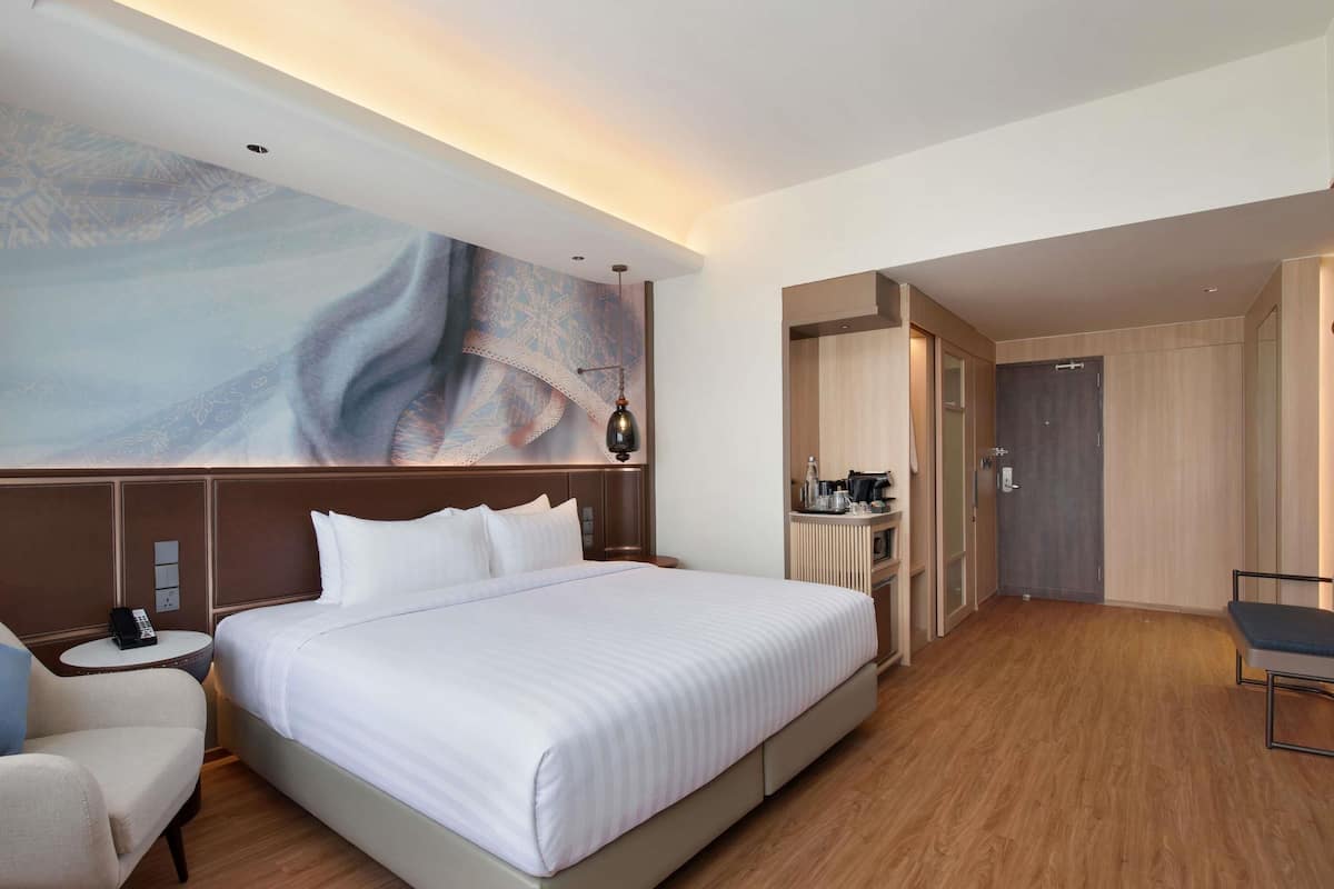 Una habitación de hotel con una cama grande, un escritorio, una silla y un cuadro en la pared.