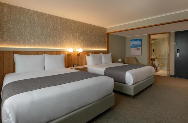 Ett hotellrum med två sängar, en sänggavel i trä, en väggmonterad lampa och en dörr som leder till ett badrum.