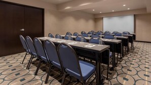 Ein Konferenzraum mit Reihen von Stühlen, Tischen und einer Projektionsleinwand.