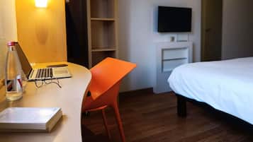 Una camera d'albergo con un letto, una scrivania con un portatile, una sedia, un televisore montato a parete e un armadio.