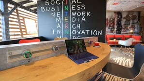 A modern workspace with a laptop on a wooden desk, a blackboard with words like "SOCIAL BUSINESS INTERNSHIP," and a red couch in the background. - ibis Aurillac (Aurillac)