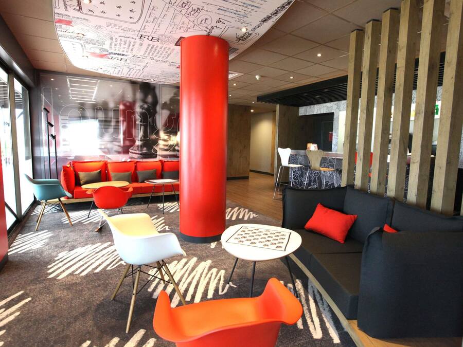 Un hall d’entrée moderne avec un pilier rouge, un canapé noir et un fauteuil bleu.