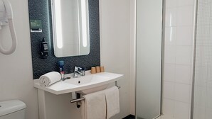 A modern bathroom with a white toilet, a sink with a mirror, and a glass-enclosed shower. - ibis Aurillac (Aurillac)