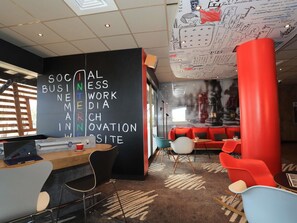 A modern office space with a blackboard listing topics like social business and innovation, a laptop on a desk, and red and blue chairs. - ibis Aurillac (Aurillac)