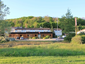 A two-story building with a flat roof, a visible entrance, and a parking area with cars. - ibis Aurillac (Aurillac)