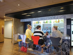 A group of people seated at a bar area with a counter and a variety of bottles on display. - ibis Aurillac (Aurillac)