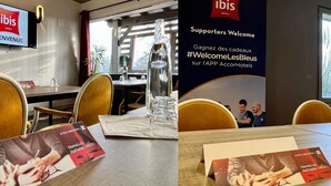 A hotel reception area with a large sign welcoming supporters, a television displaying the hotel's name, and brochures on the table. - ibis Aurillac (Aurillac)